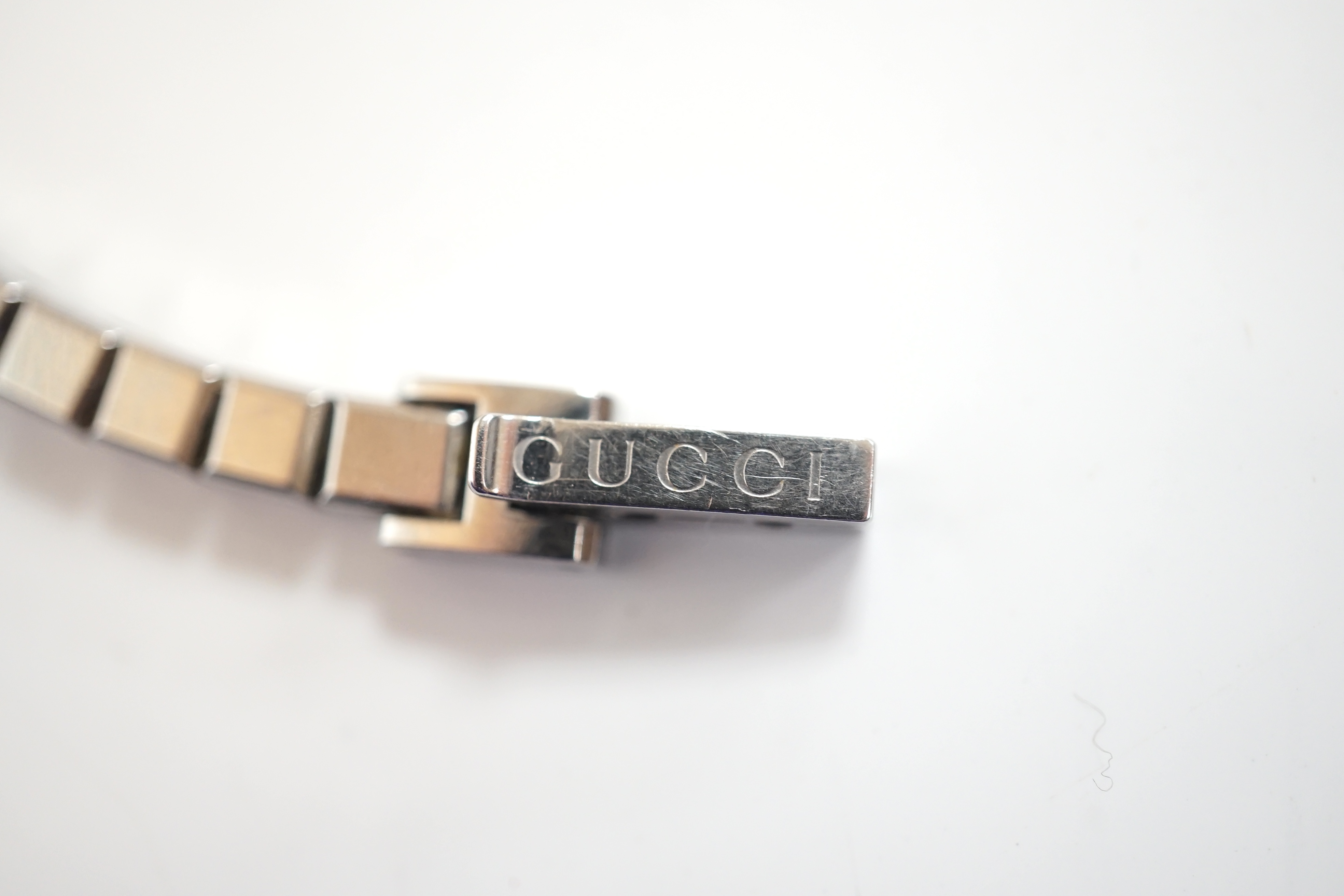 A lady's stainless steel Gucci quartz wrist watch, with G shaped case and diamond chip set bezel, on a stainless steel Gucci bracelet. Condition - fair